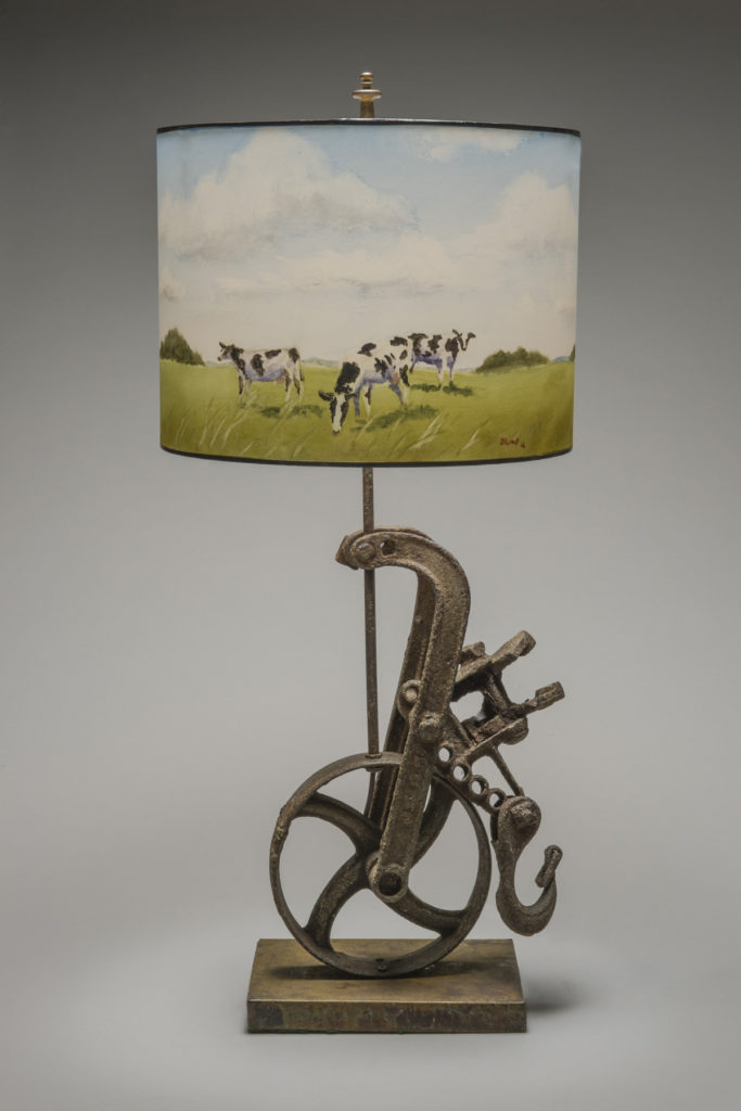 A painted lampshade by Stamp depicting cows, mounted on a plow shape