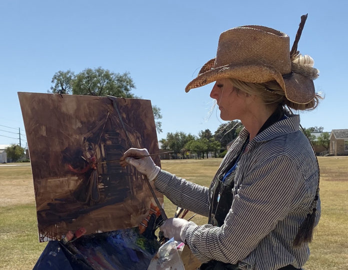 Krystal W. Brown painting one last piece during the Chuck Wagon Brunch at the 2019 EnPleinAirTEXAS event at Fort Concho in San Angelo. Photo by Hiu Lai Chong. Woman painting outdoors in a hat