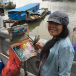 Plein air artist Hai-Ou Hou painting outside in China next to a river.
