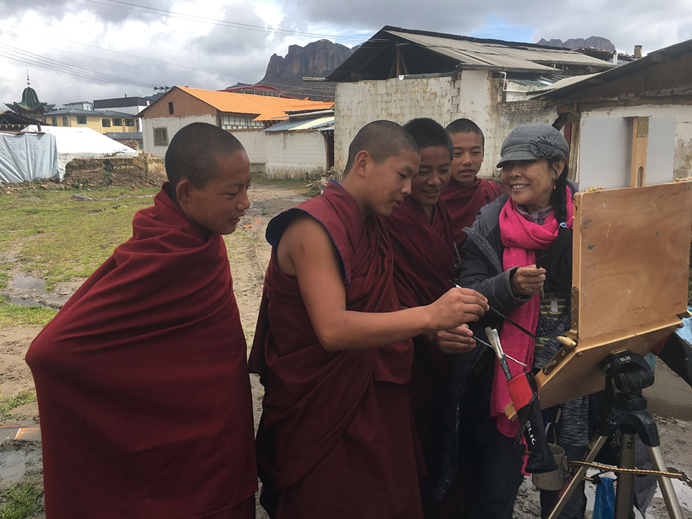 Artist painting outdoors while Tibetan men watch