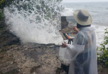 Woman artist painting outdoors right near crashing waves