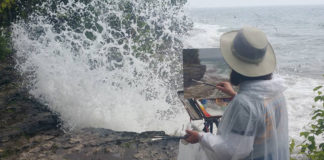 Woman artist painting outdoors right near crashing waves