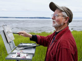 Male artist painting outdoors near a body of water