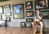 Artist sitting in his studio with framed paintings filling the wall