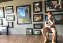 Artist sitting in his studio with framed paintings filling the wall