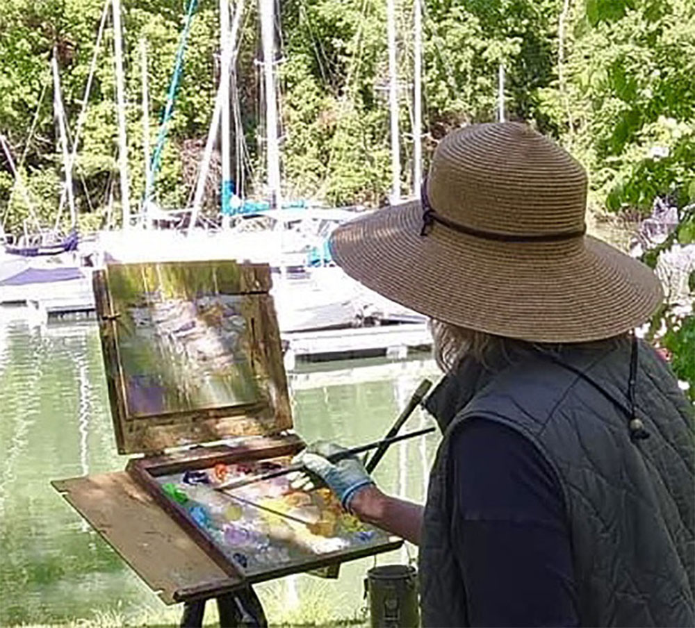 Woman painting sailboats outdoors at a marina