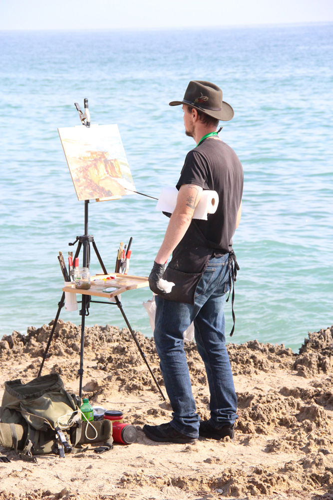 Man painting on rocks overlooking the ocean