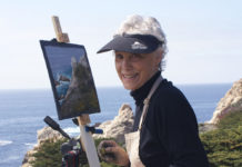 Photo of a female artist painting on a bluff by the ocean