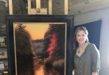 Female artist standing in front of a large painting on an easel in her studio