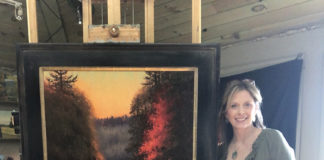 Female artist standing in front of a large painting on an easel in her studio