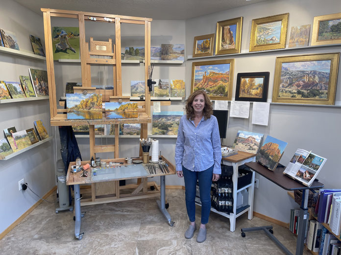 Female artist in her studio with easel and paintings on the walls