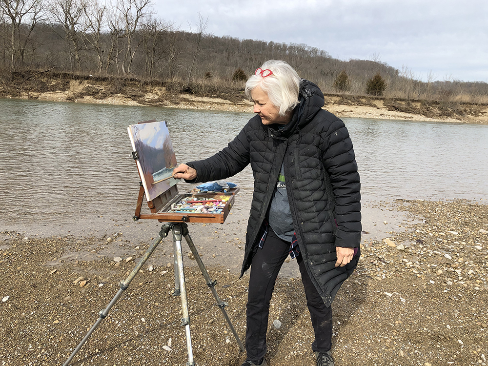 Female artist painting outdoors by a body of water