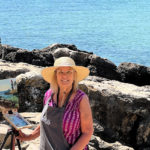 artist Kathleen posing for a photograph in front of ocean view painting