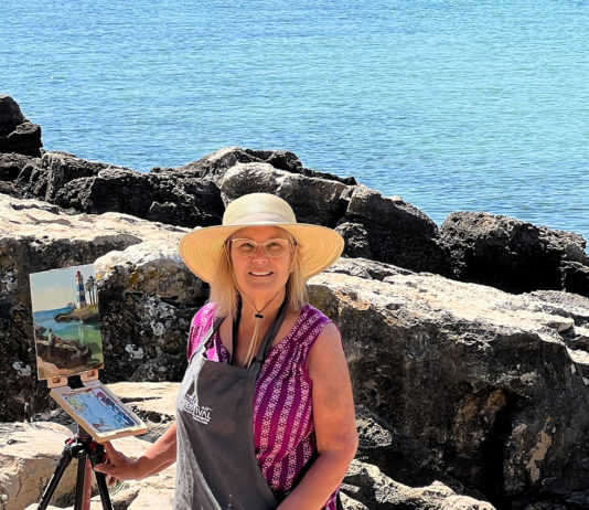 artist Kathleen posing for a photograph in front of ocean view painting