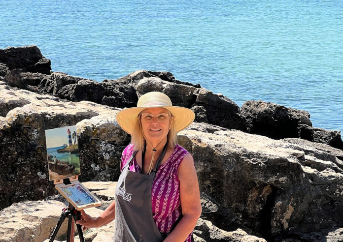 artist Kathleen posing for a photograph in front of ocean view painting