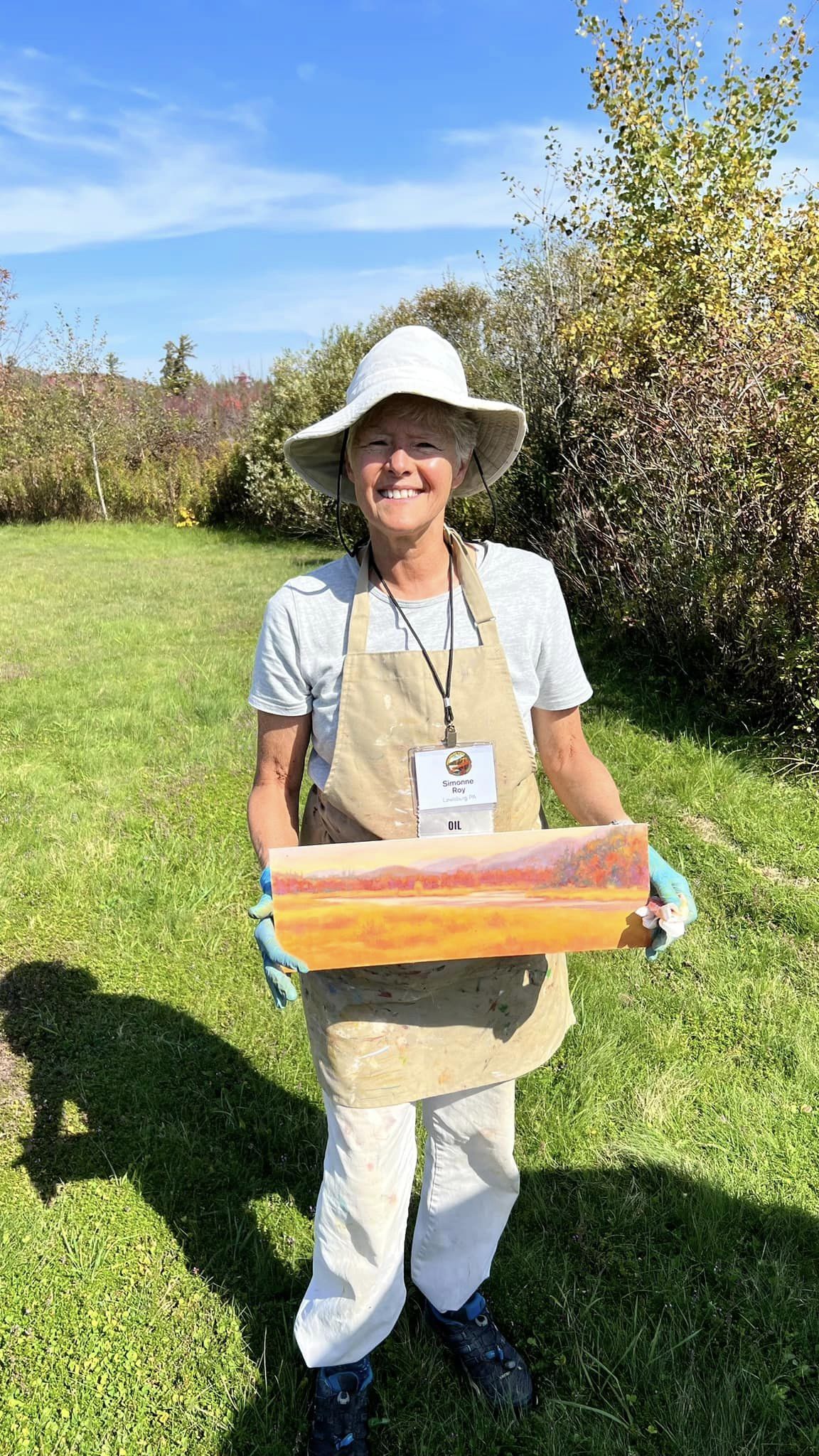 Simonne Roy holding up one of her plein air paintinggs