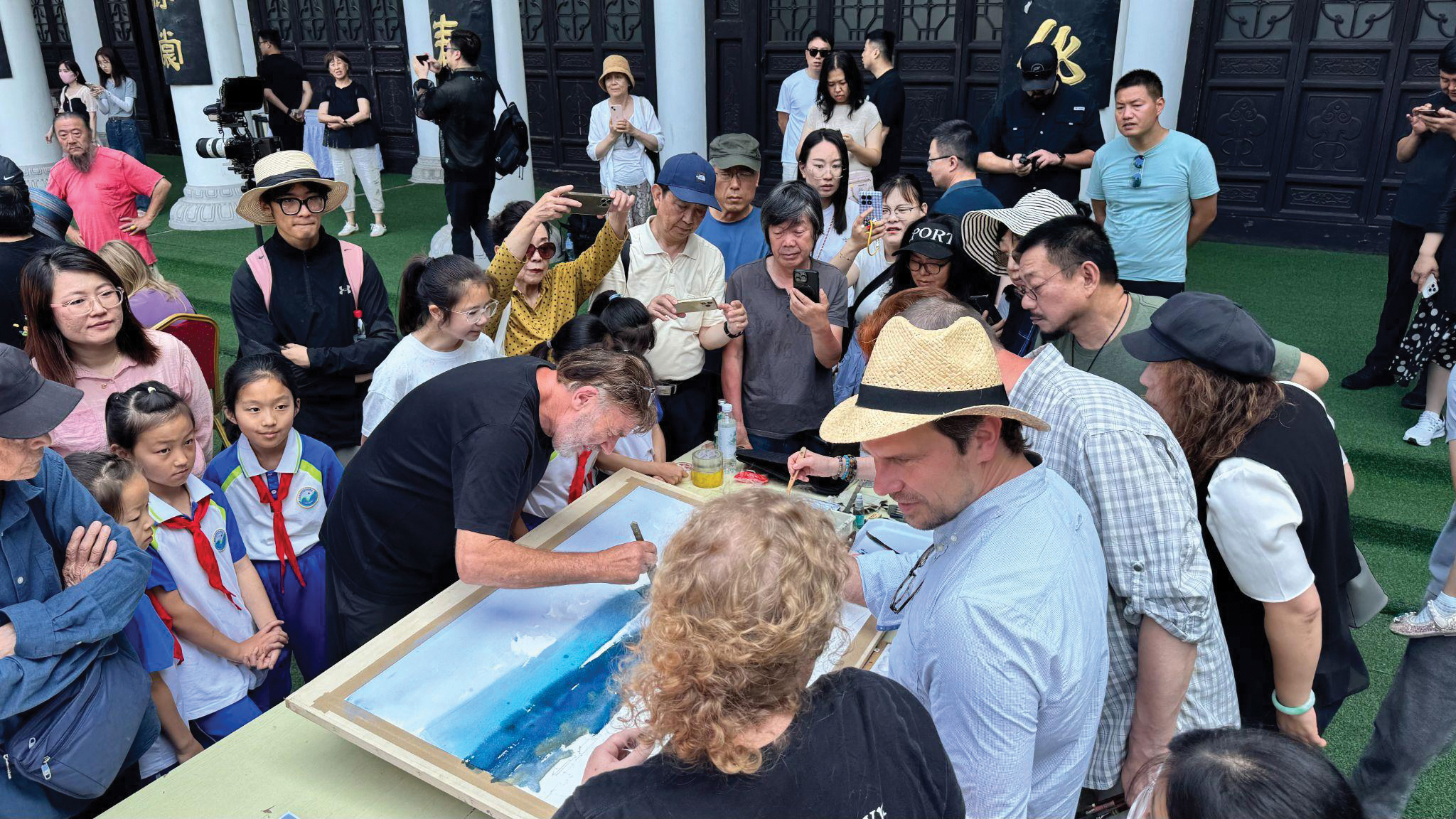 A crowd gathered to observe artists working on a group painting.
